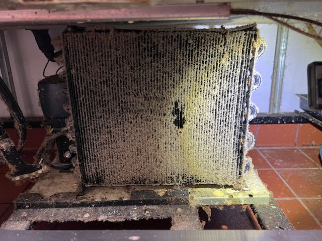 A dirty refrigerator coil is sitting on top of a tiled floor.