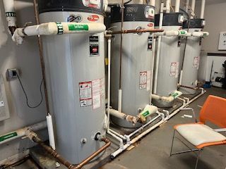 A row of water heaters are lined up in a room next to a chair.