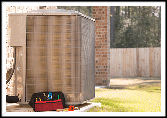An air conditioner is sitting on the side of a building next to a tool bag.
