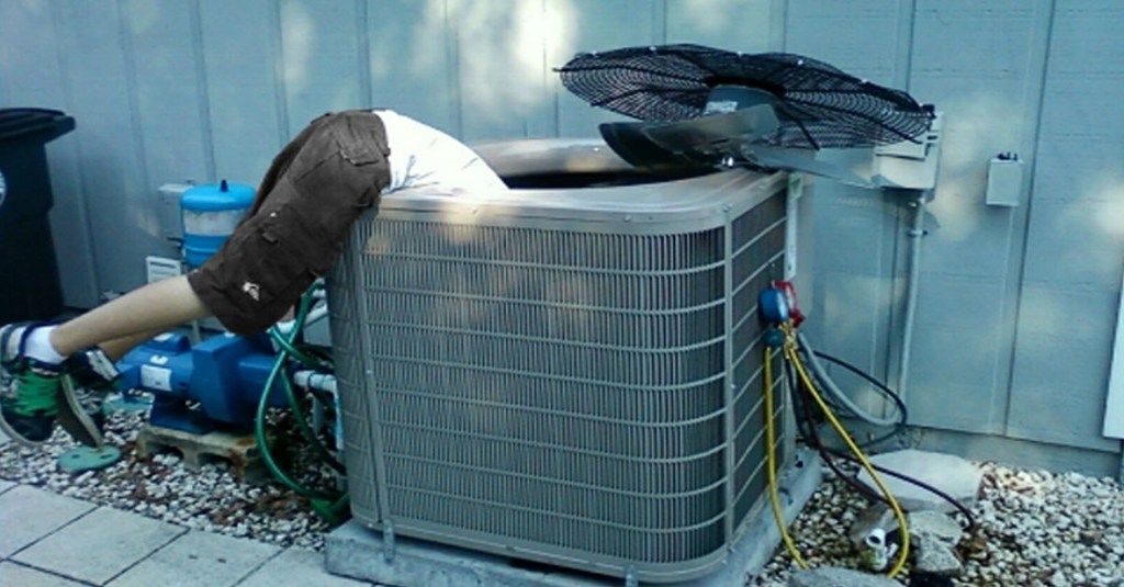 A man is laying on top of an air conditioner.