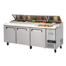 A stainless steel salad prep counter with a pizza on top of it.