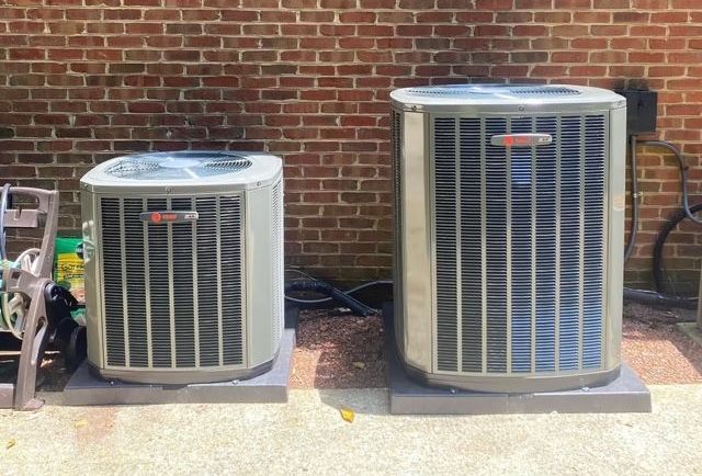 Two air conditioners are sitting next to each other in front of a brick wall.