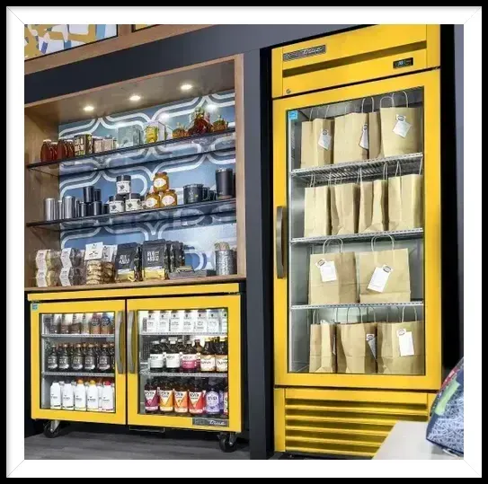 A yellow refrigerator filled with bags and bottles in a store.