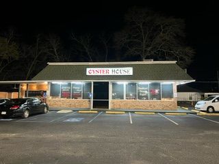A oyster house restaurant is lit up at night with cars parked in front of it.
