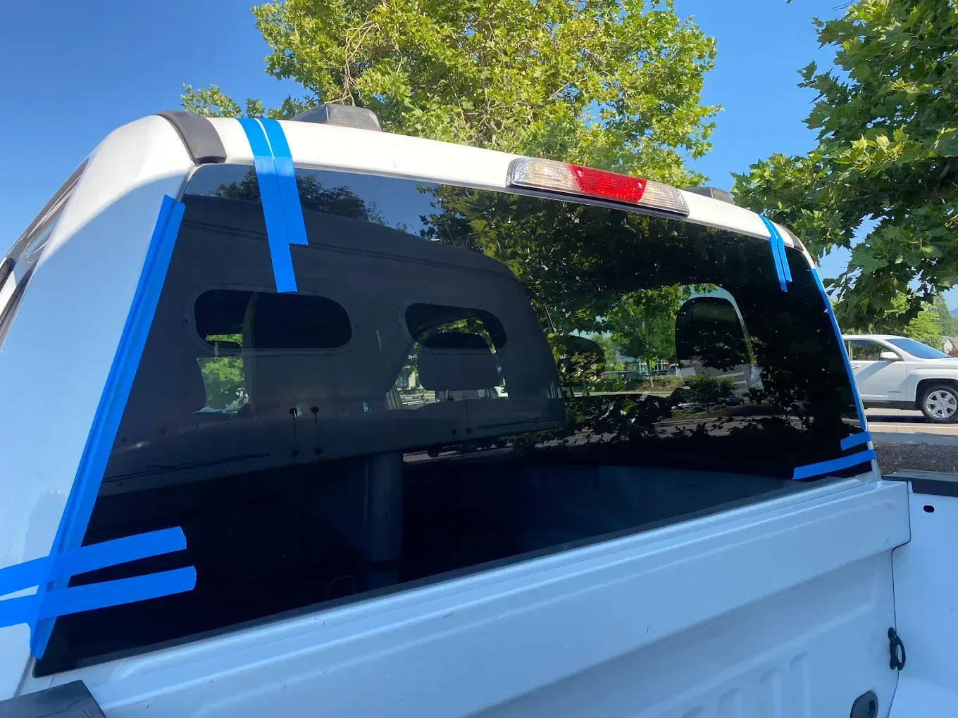 White pickup truck with blue tape around the rear window, possibly for tinting or repair.