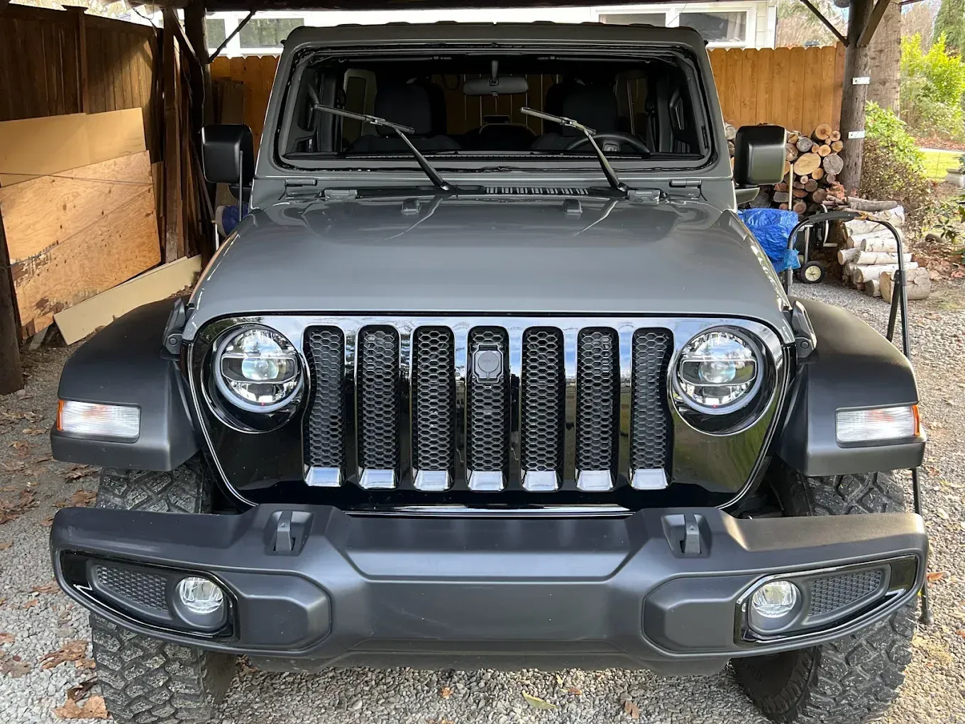 Gray Jeep Wrangler parked under a wooden carport.