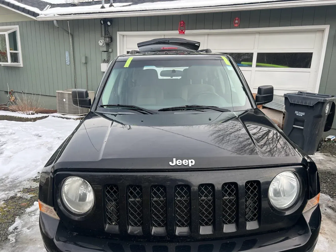 Black Jeep Patriot parked in front of a light green house with snow on the ground.