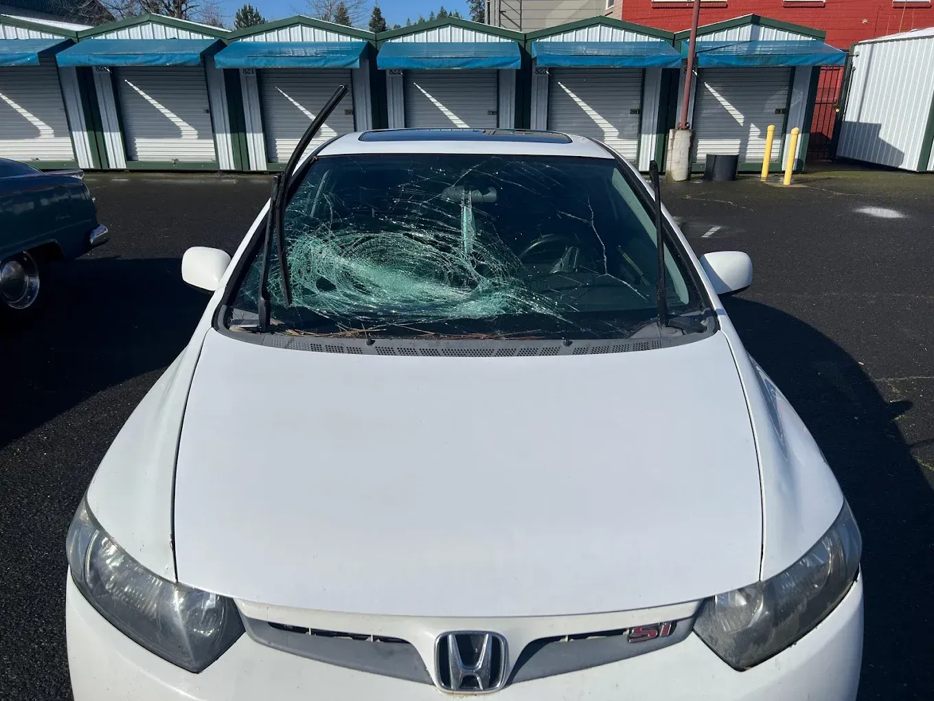 White Honda Civic with heavily damaged windshield, parked outdoors.