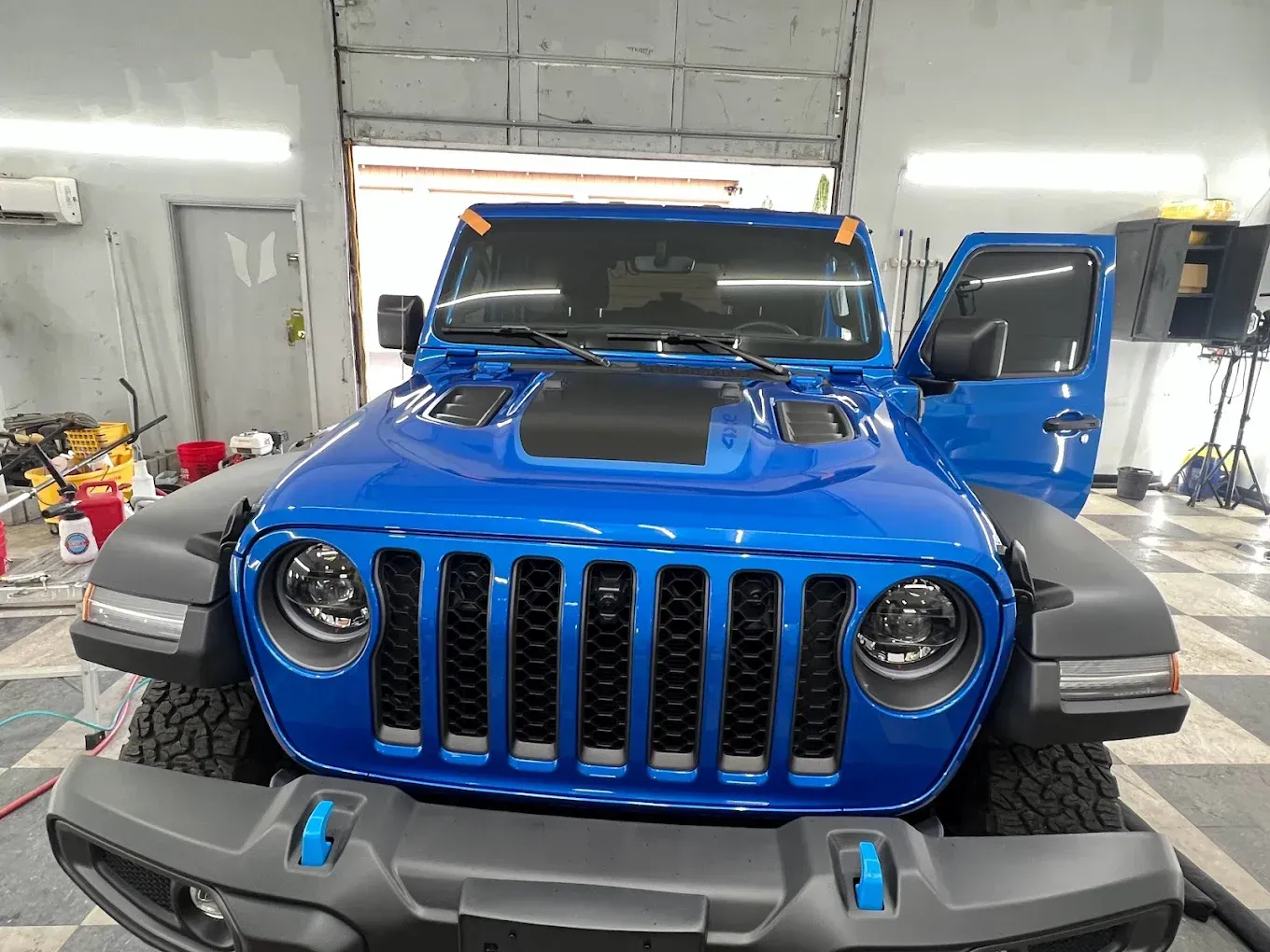 Blue Jeep Wrangler parked in a garage with door open.