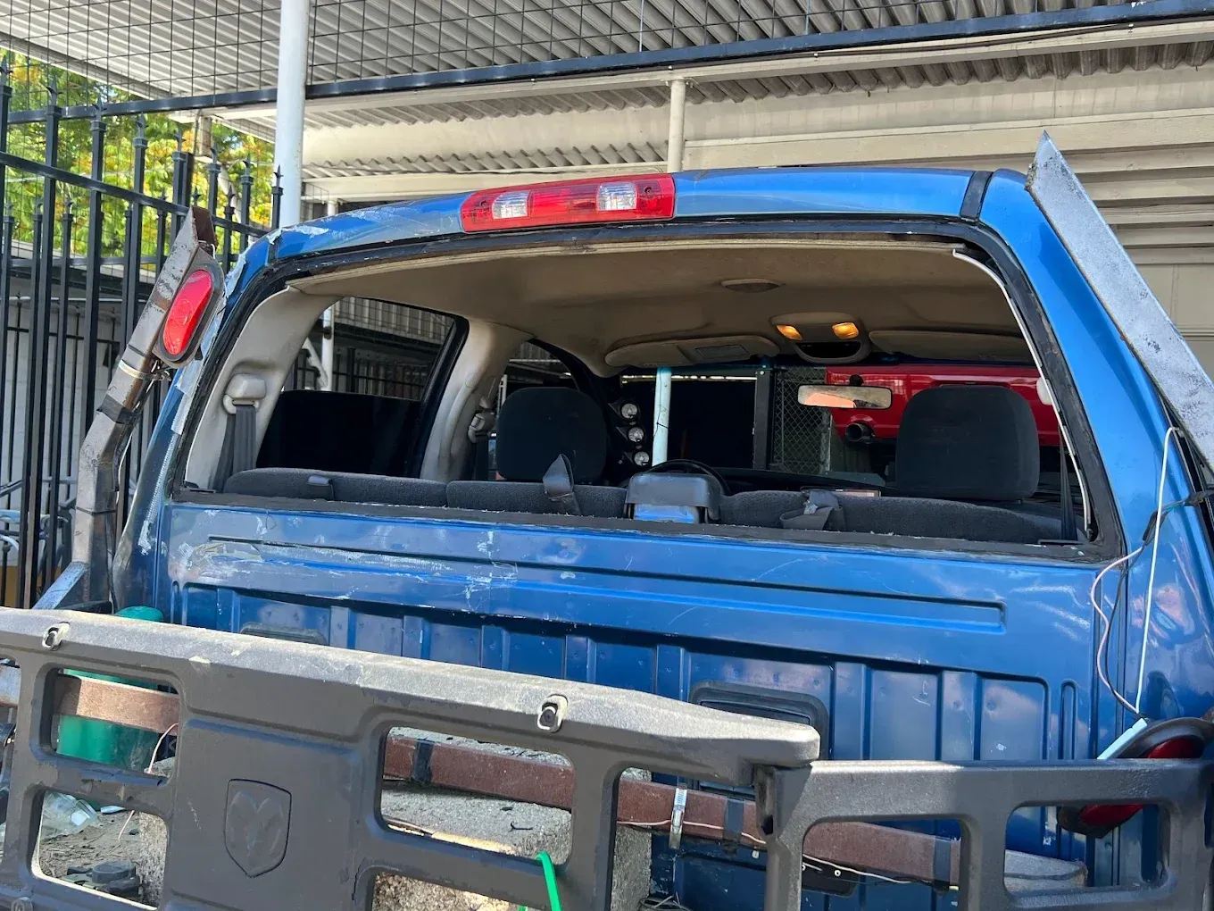 Blue pickup truck with rear window broken out, debris in the bed, parked outdoors.