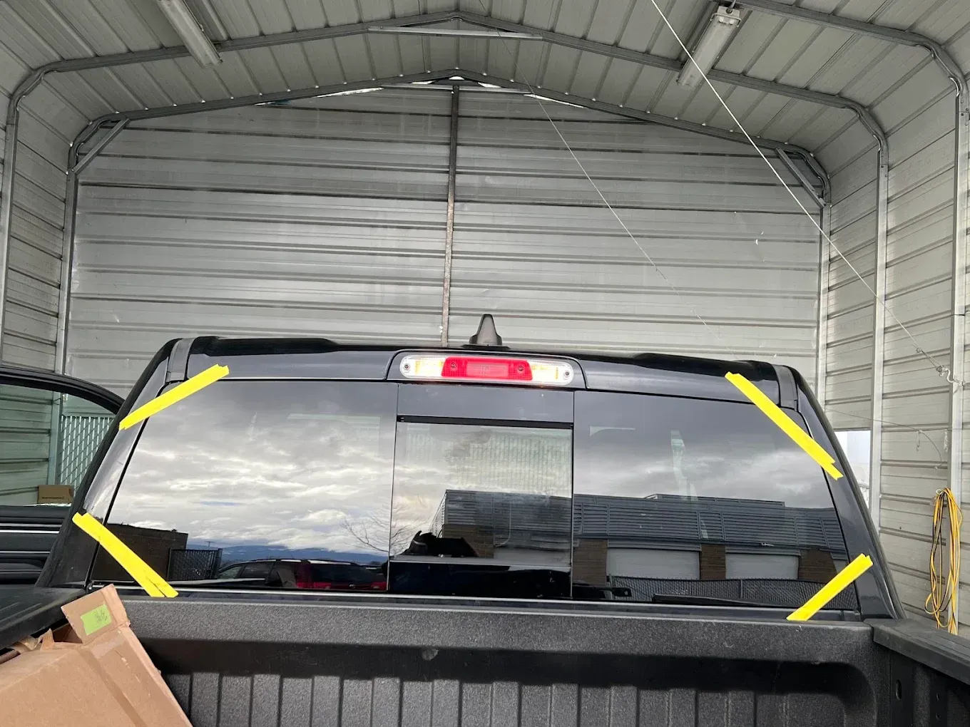 Black truck's rear window with yellow tape inside a metal storage building.