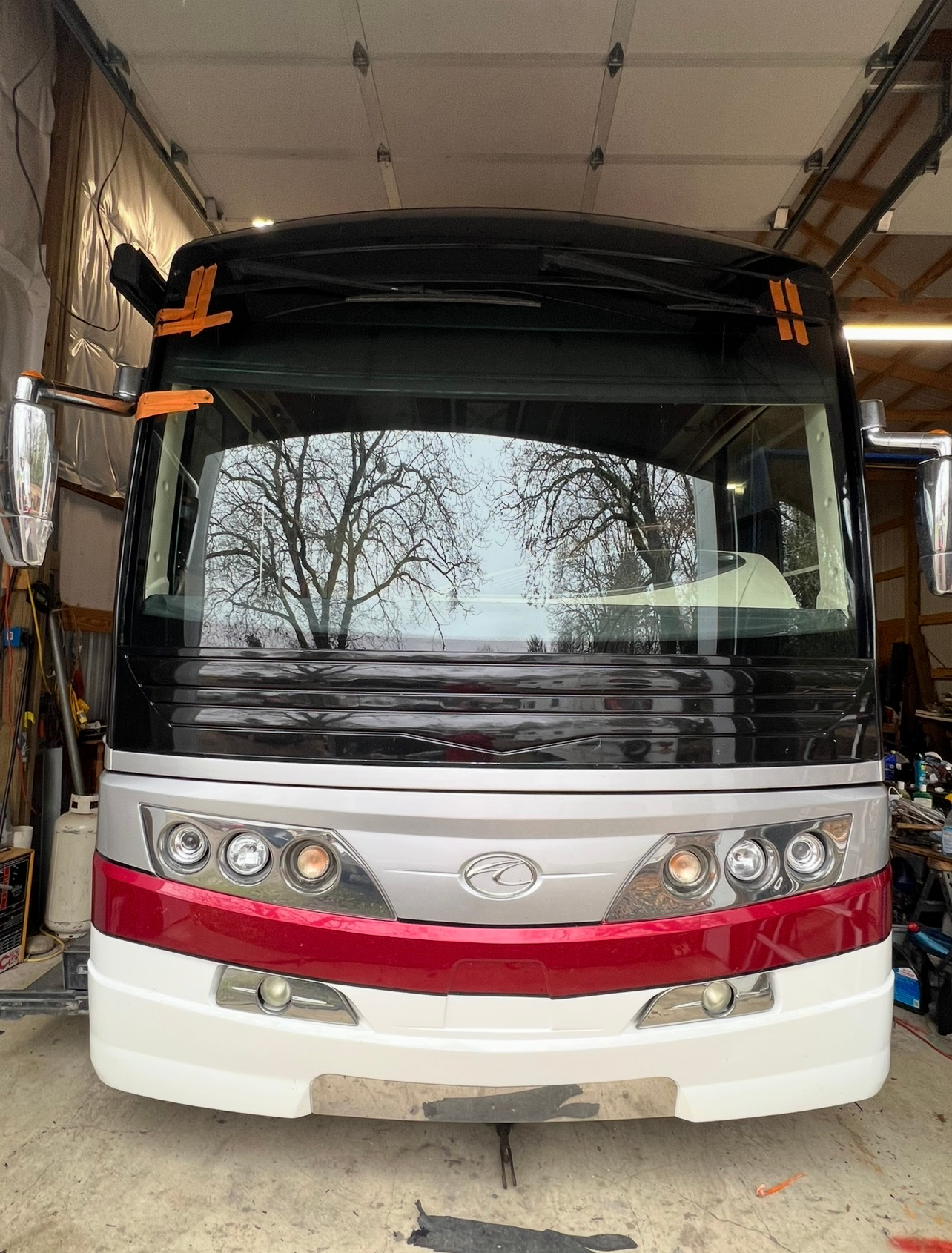 Man working on a black RV windshield with the window removed, outdoors on a sunny day.