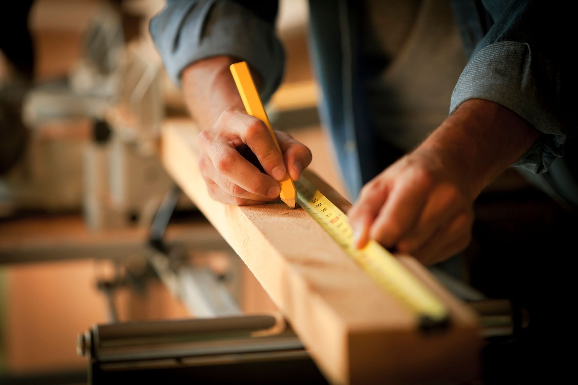 A man is measuring a piece of wood with a tape measure.