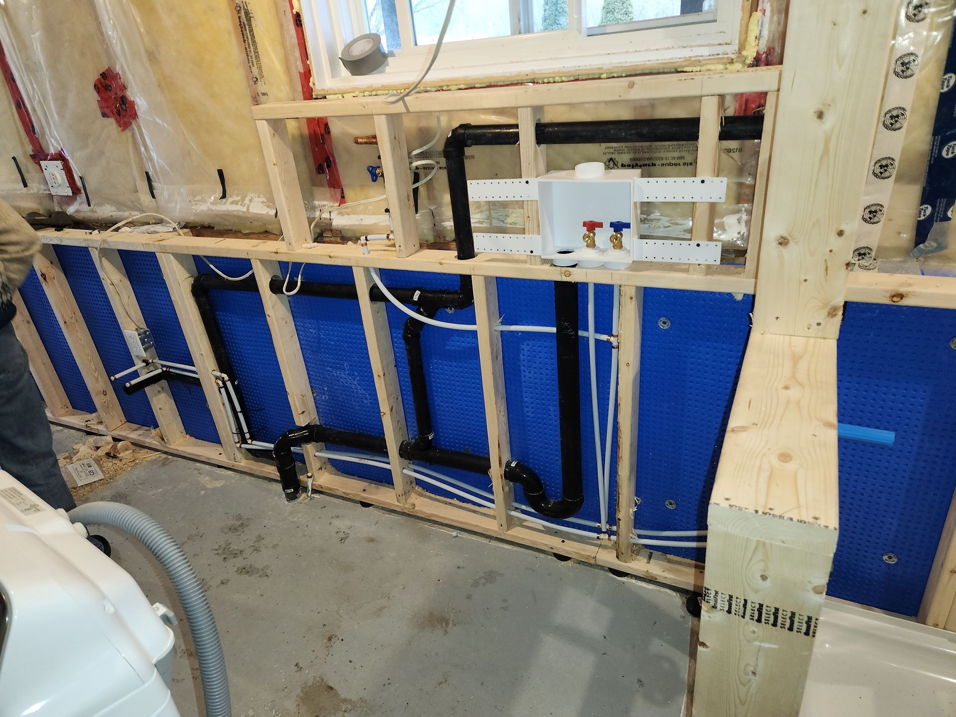 Framed-out wall with plumbing. Blue insulation, black pipes, and a water supply box.