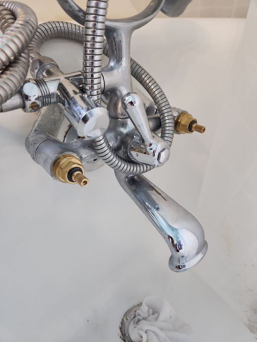Chrome bathtub faucet with attached shower hose and spigot, over a white tub.