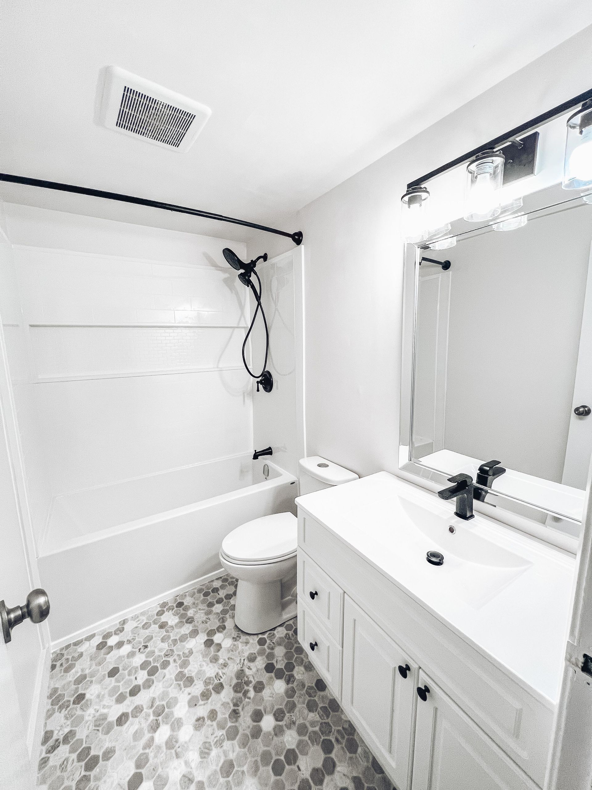 Bathroom with white fixtures, black hardware, gray and white tile floor.