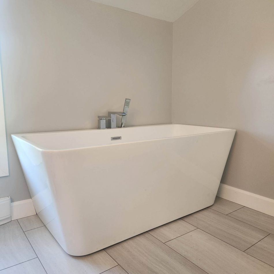 White rectangular soaking tub in a bathroom corner, chrome faucet, light gray walls and flooring.