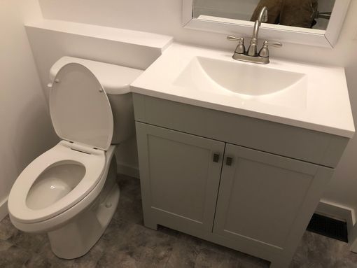 Bathroom with white toilet, vanity, and sink, set against a light-colored wall.