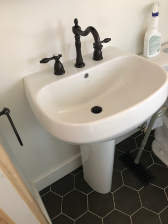 White pedestal sink with dark fixtures, set against a white wall and dark hexagon tile floor.