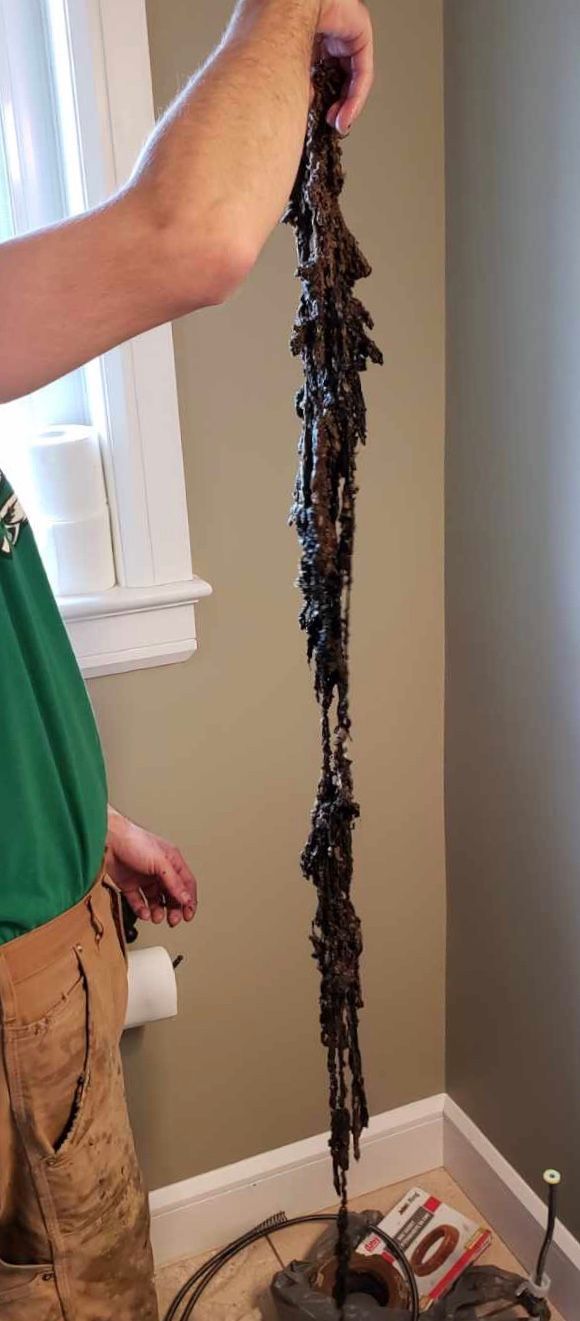 Person holding a dark, ornate light fixture. Brown pants, green shirt, beige wall, window.