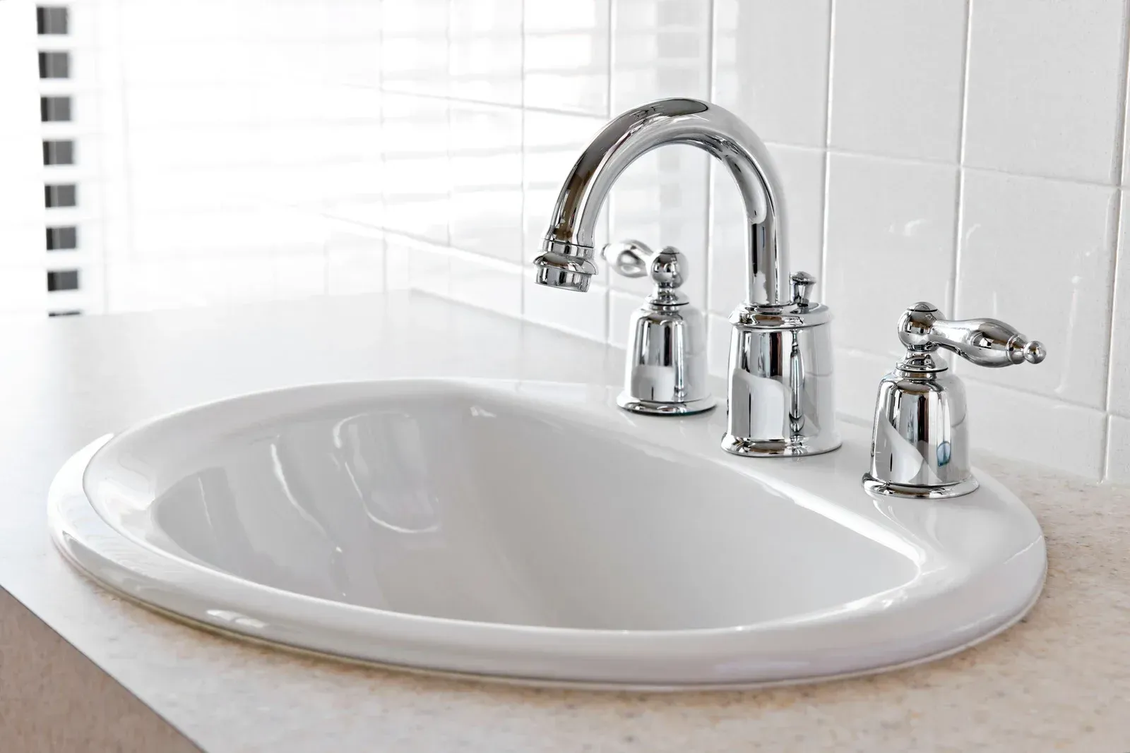 White oval bathroom sink with chrome faucet and handles.