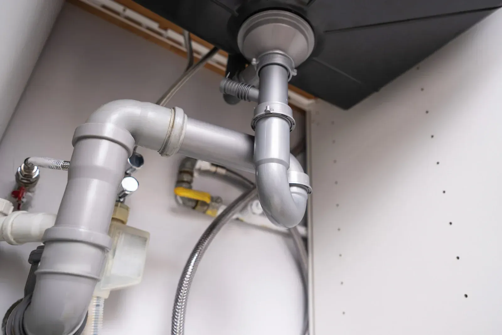 Gray plumbing pipes under a sink in a white cabinet.