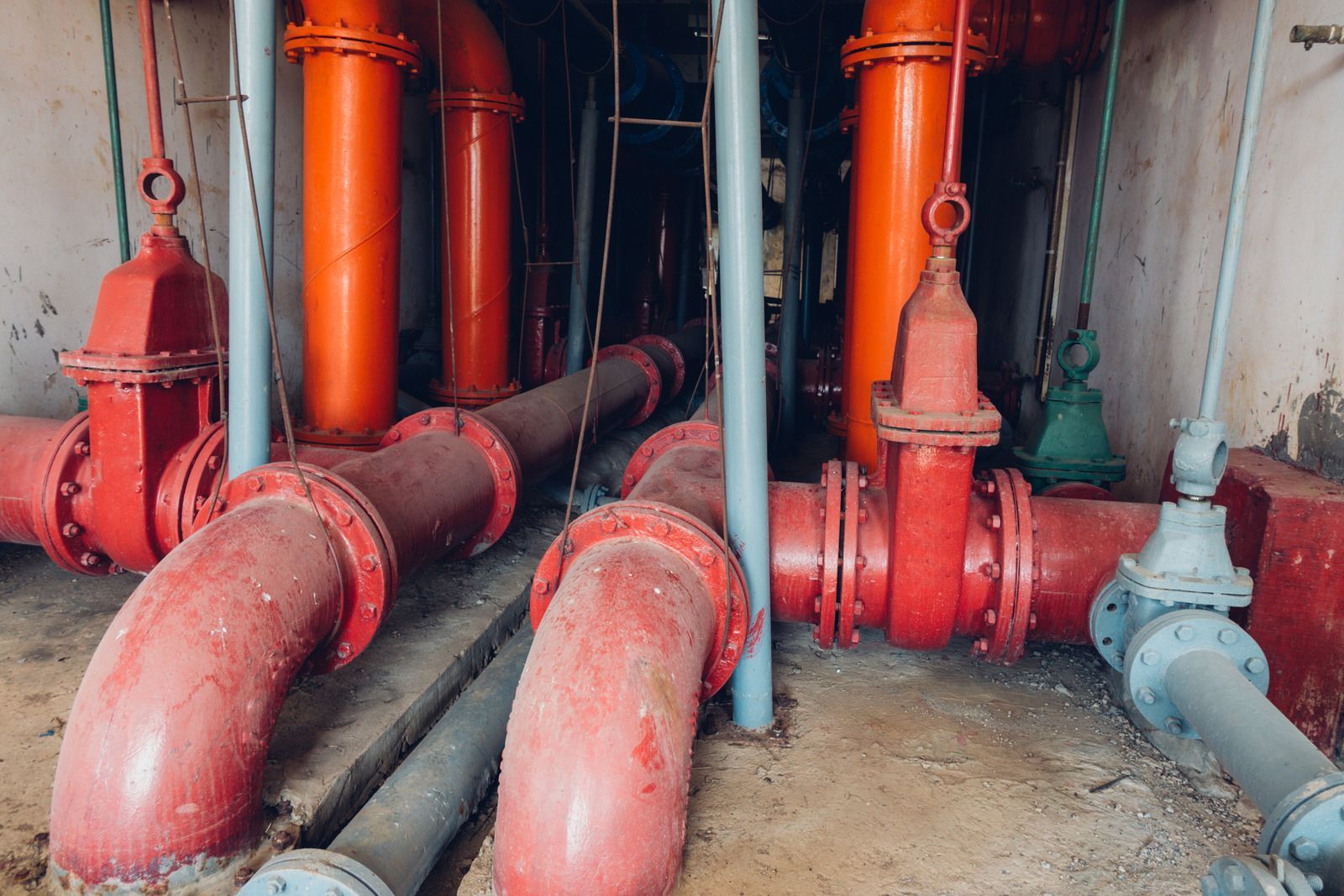 Red and orange pipes with valves in a concrete room, likely for water or industrial use.