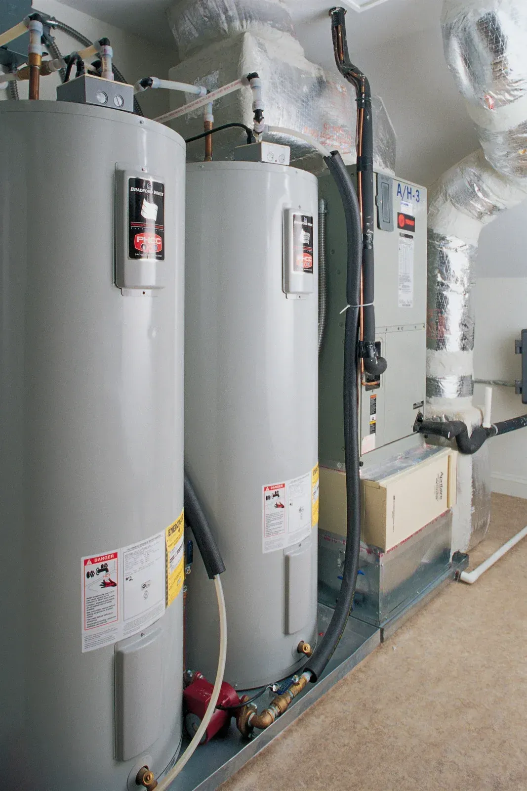 Two gray water heaters and a furnace in a utility room.