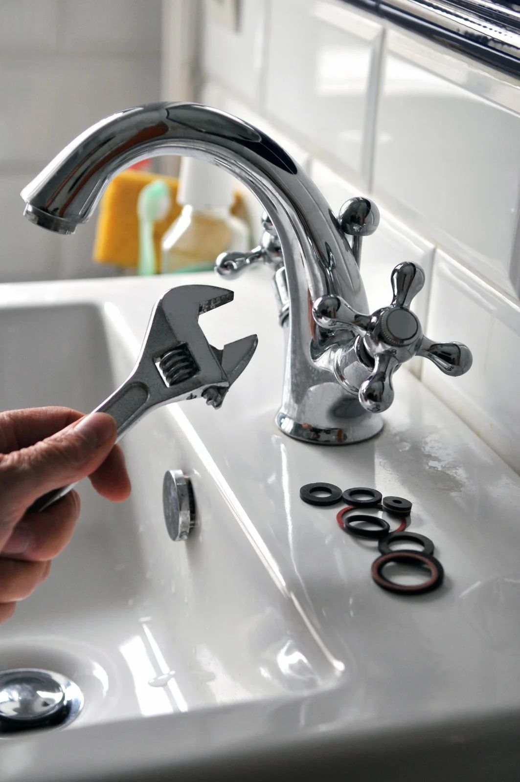Hand holding wrench, repairing chrome faucet in a white sink, with replacement washers.