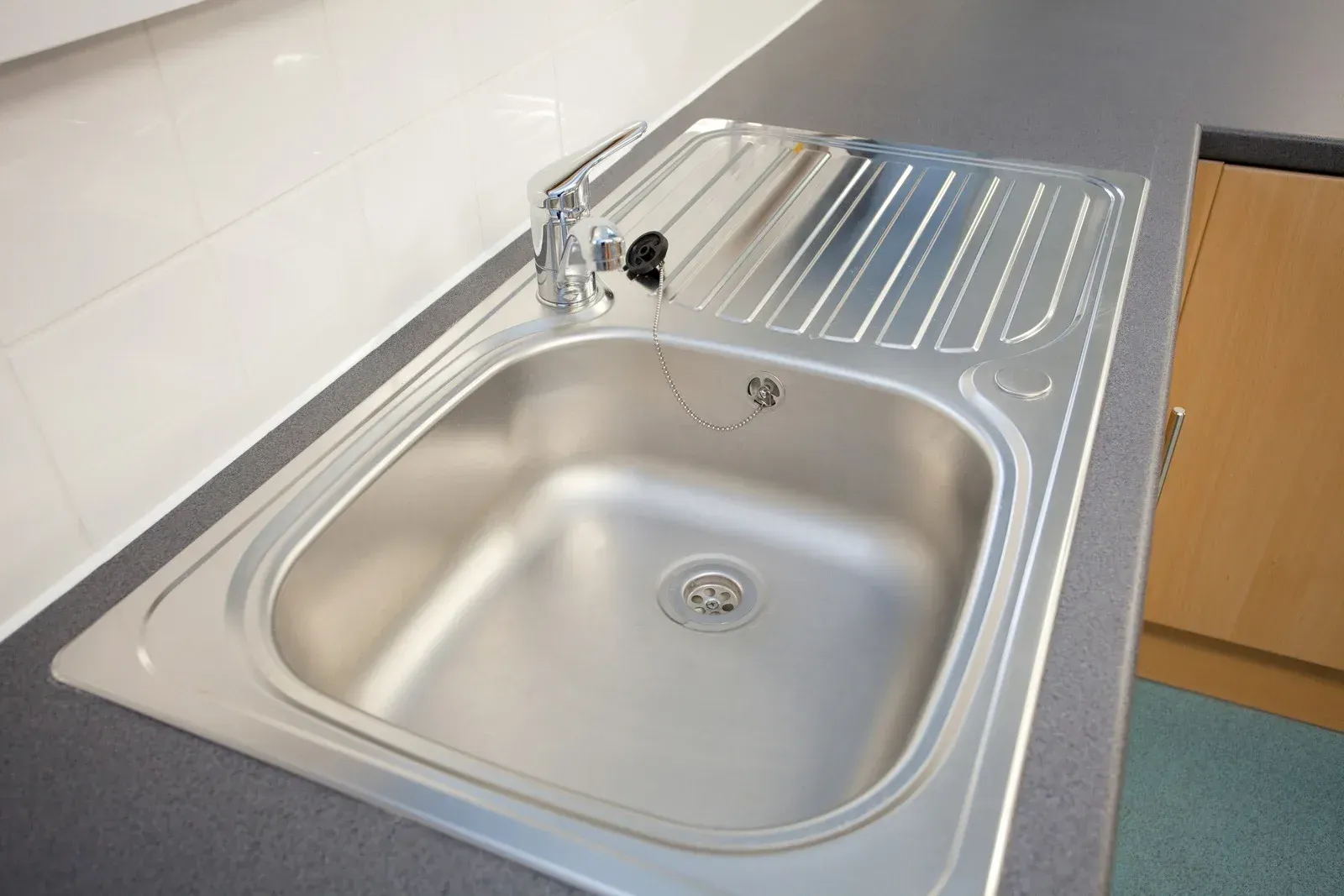 Stainless steel kitchen sink with built-in drainboard, faucet, and dark countertop.