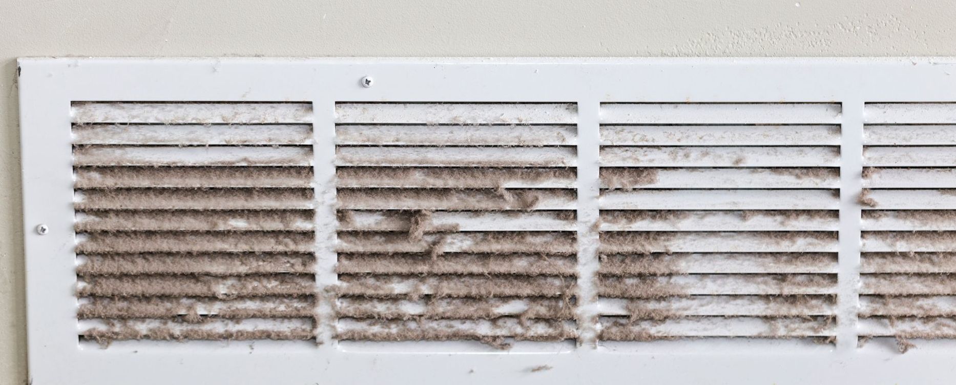 A dirty air vent on a wall next to a wooden shelf.