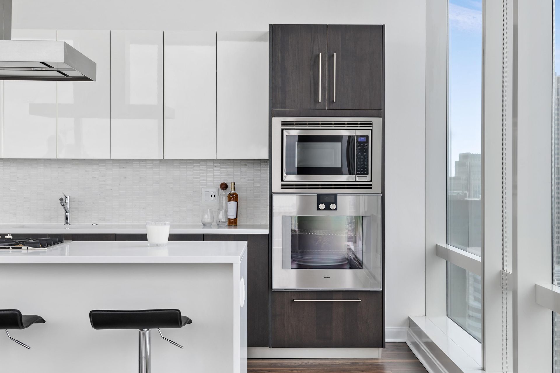 Modern kitchen featuring a white island, dark wood built-in wall oven and microwave unit, and high-rise window view.
