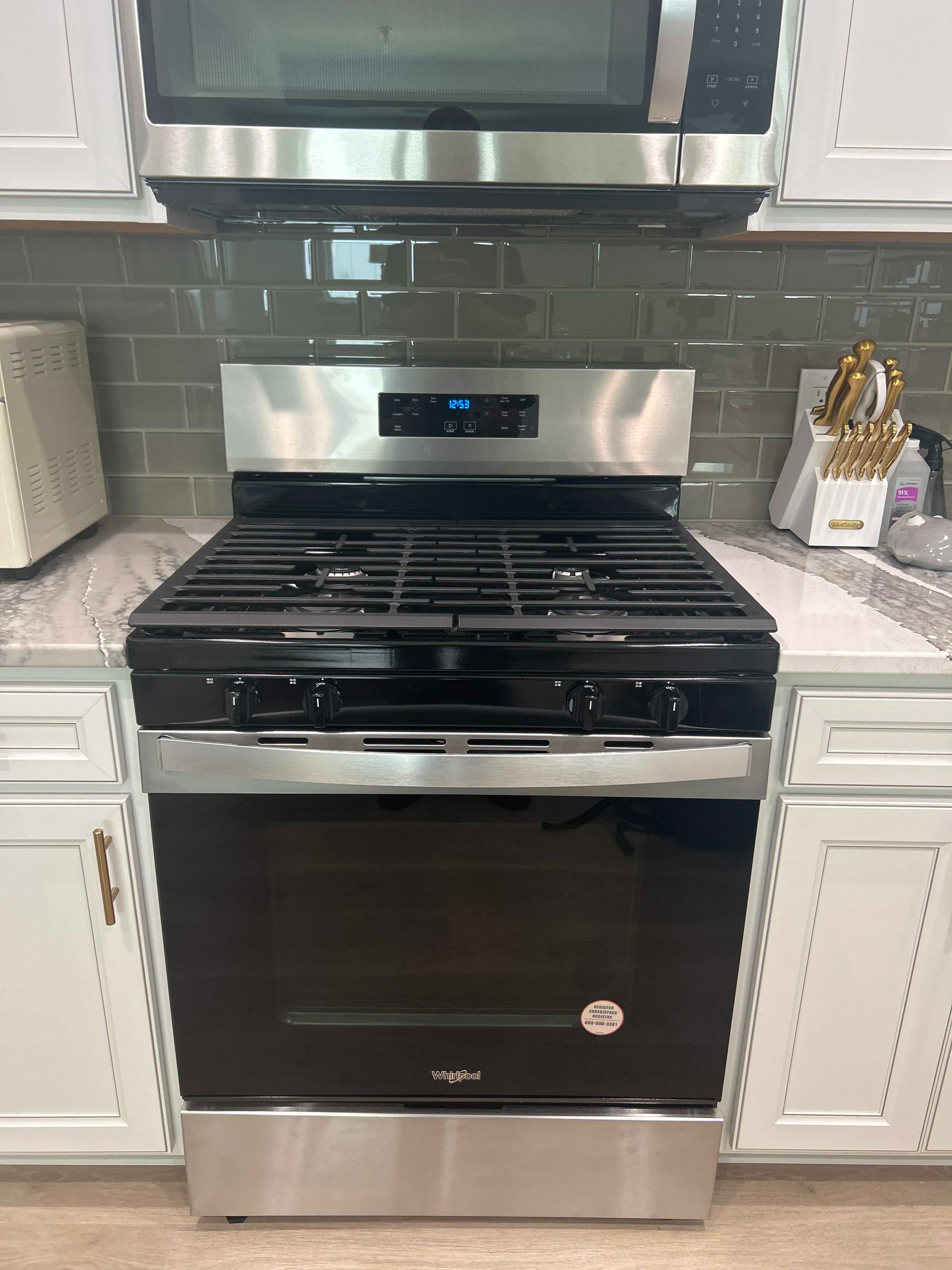 A stainless steel gas stove with a black oven door sits between white kitchen cabinets, below a matching microwave.