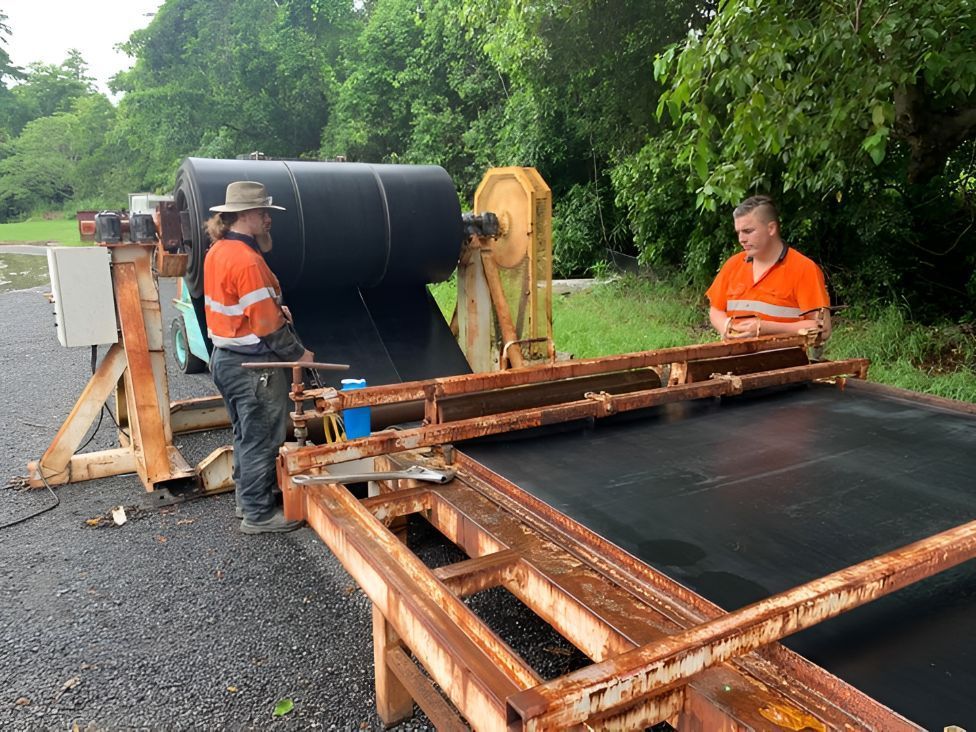 Two Men Are Working On A Conveyor Belt In A Field — Belt Maintenance & Supplies Pty Ltd In Nindaroo, QLD