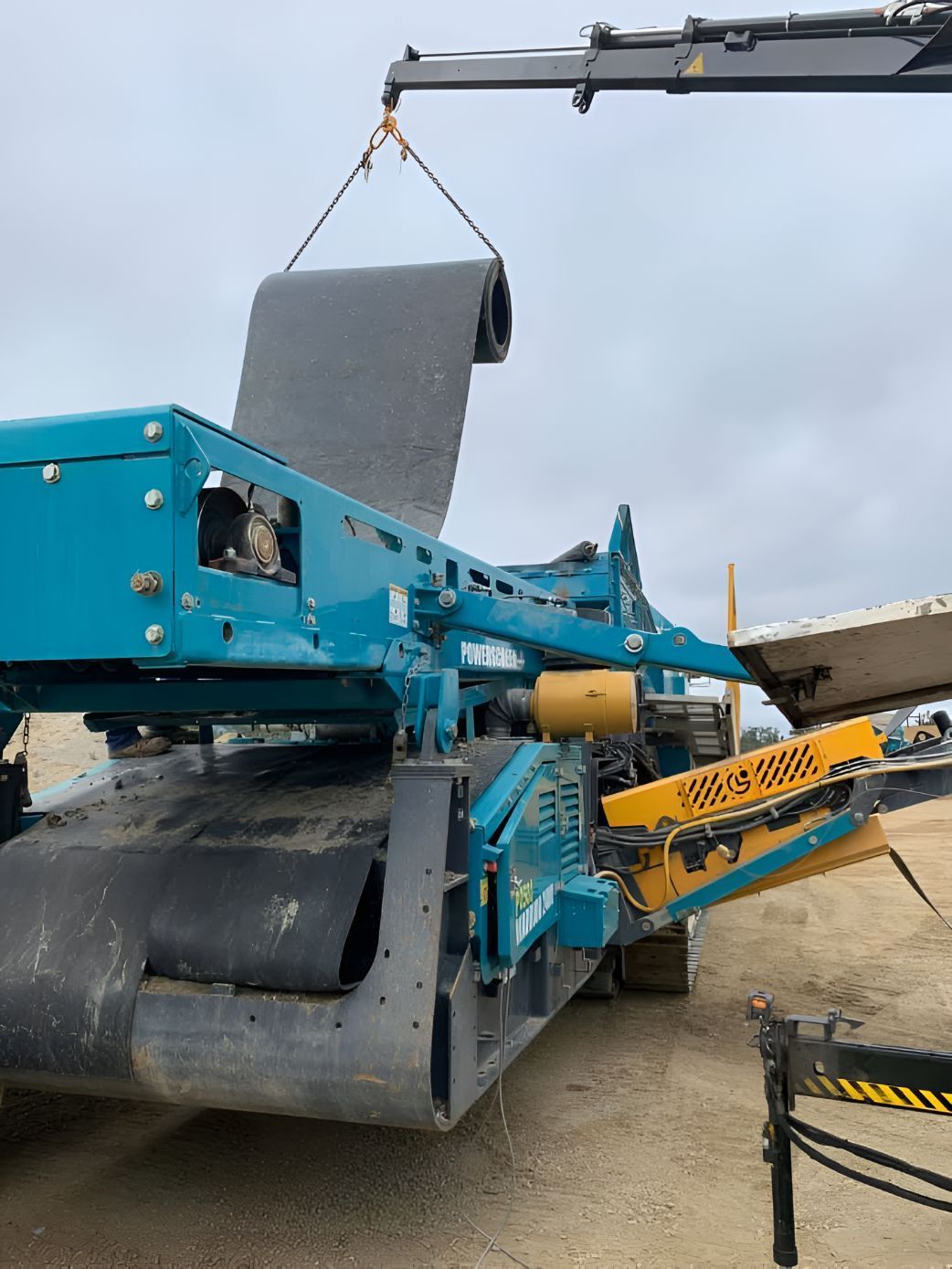 A Blue And Yellow Machine Is Being Lifted By A Crane — Belt Maintenance & Supplies Pty Ltd In Nindaroo, QLD
