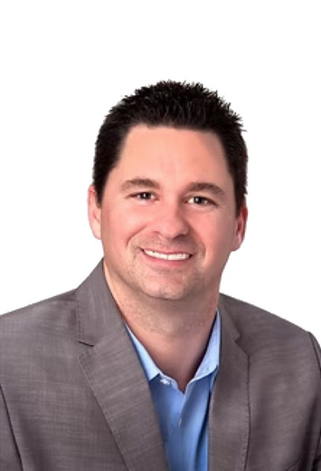 Man in gray blazer, blue shirt, smiling against a white background.
