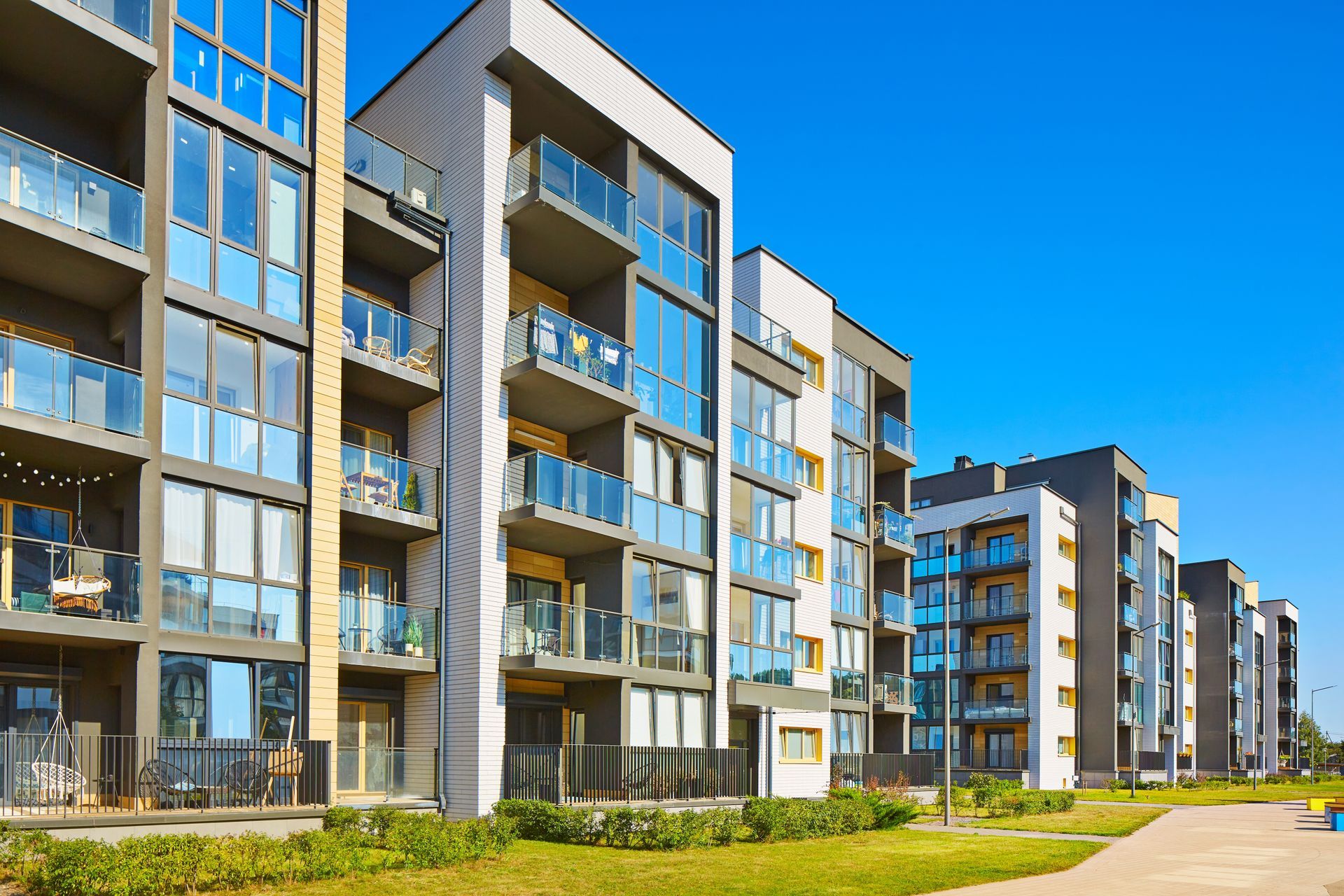 Modern apartment buildings with glass balconies, blue sky.