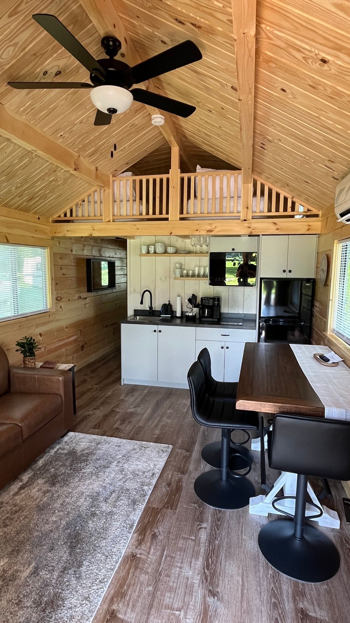 A living room and kitchen in a cabin with a ceiling fan.