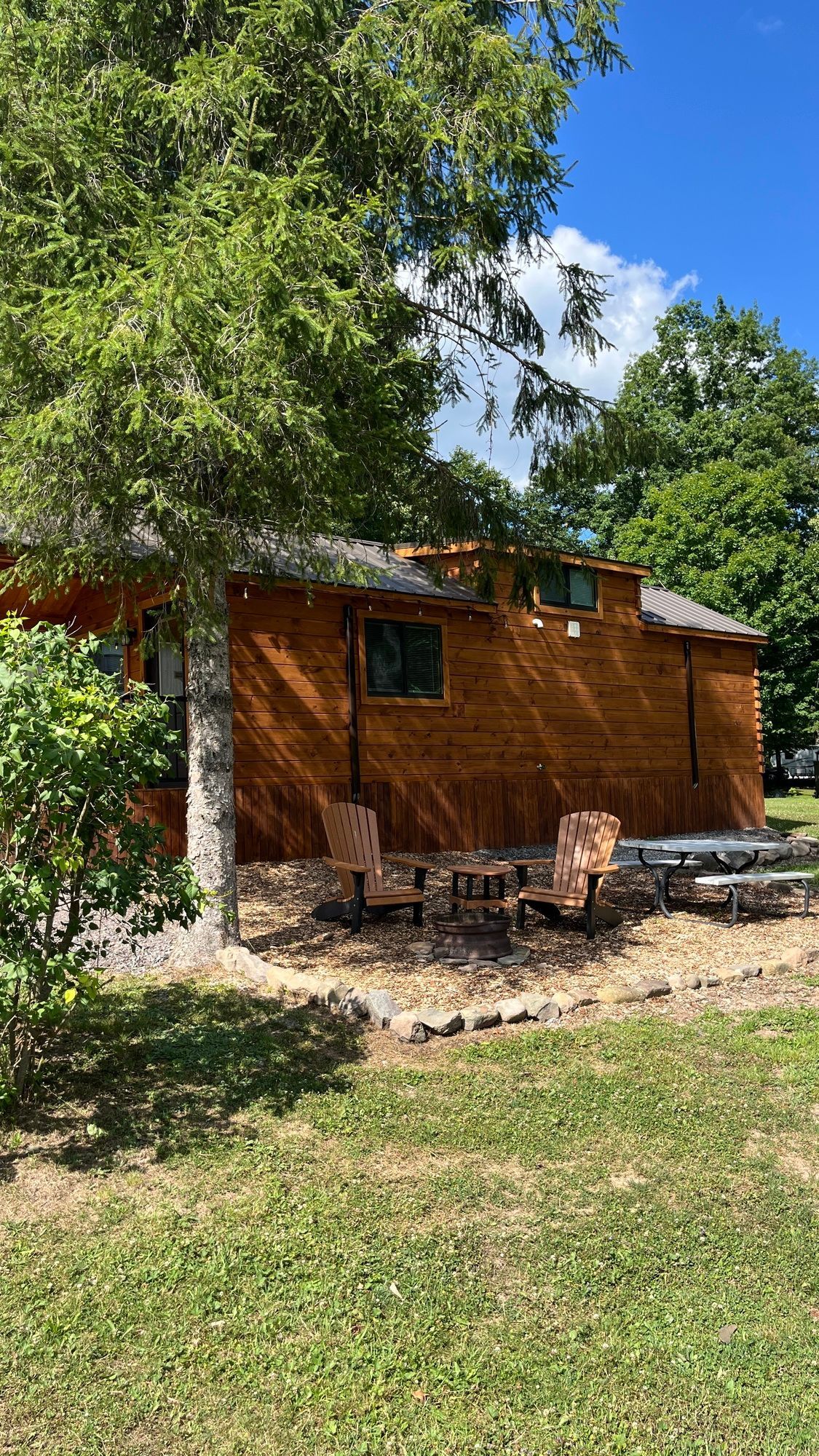 A wooden cabin is sitting in the middle of a lush green field surrounded by trees.