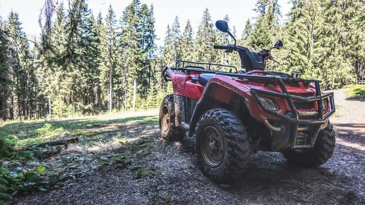 A red atv is parked on a gravel road in the woods.