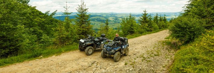 Two atvs are parked on a dirt road in the woods.
