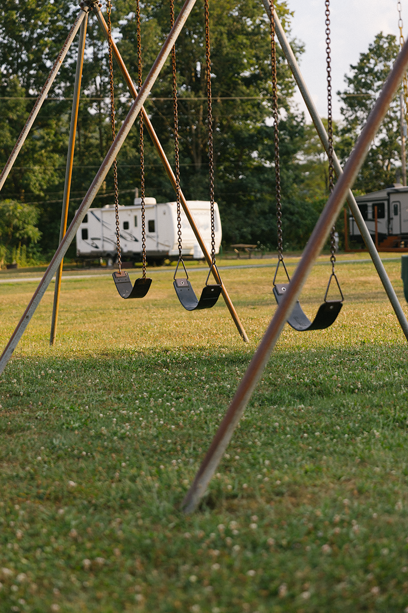 A row of swings in a field with a trailer in the background