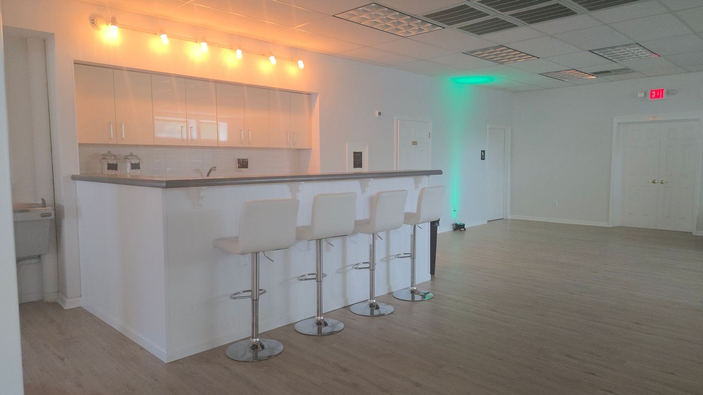A kitchen with a bar , stools , a freezer and a trash can.