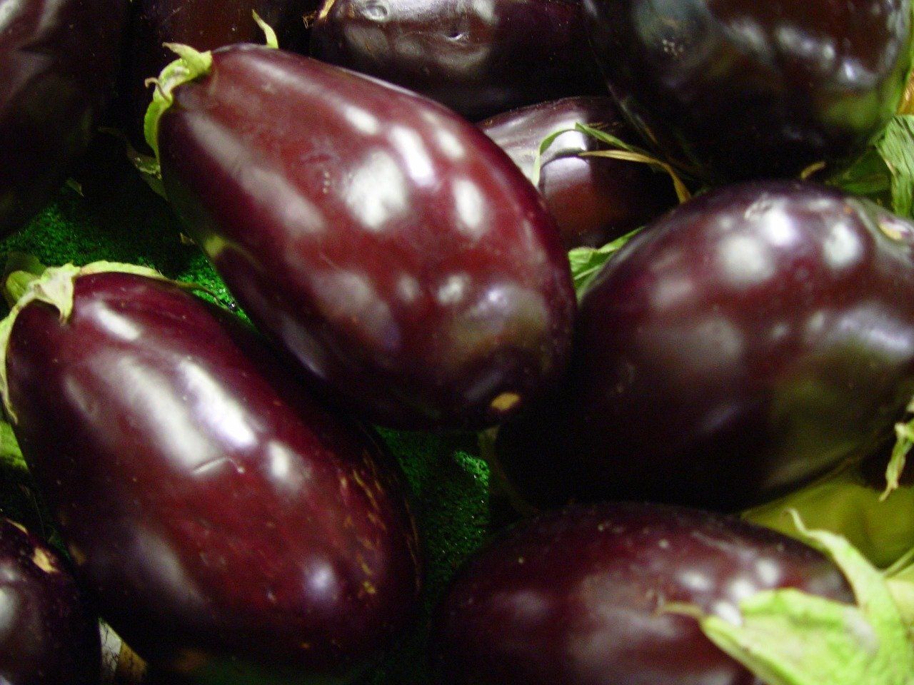 A bunch of purple eggplant sitting on top of each other on a green surface.