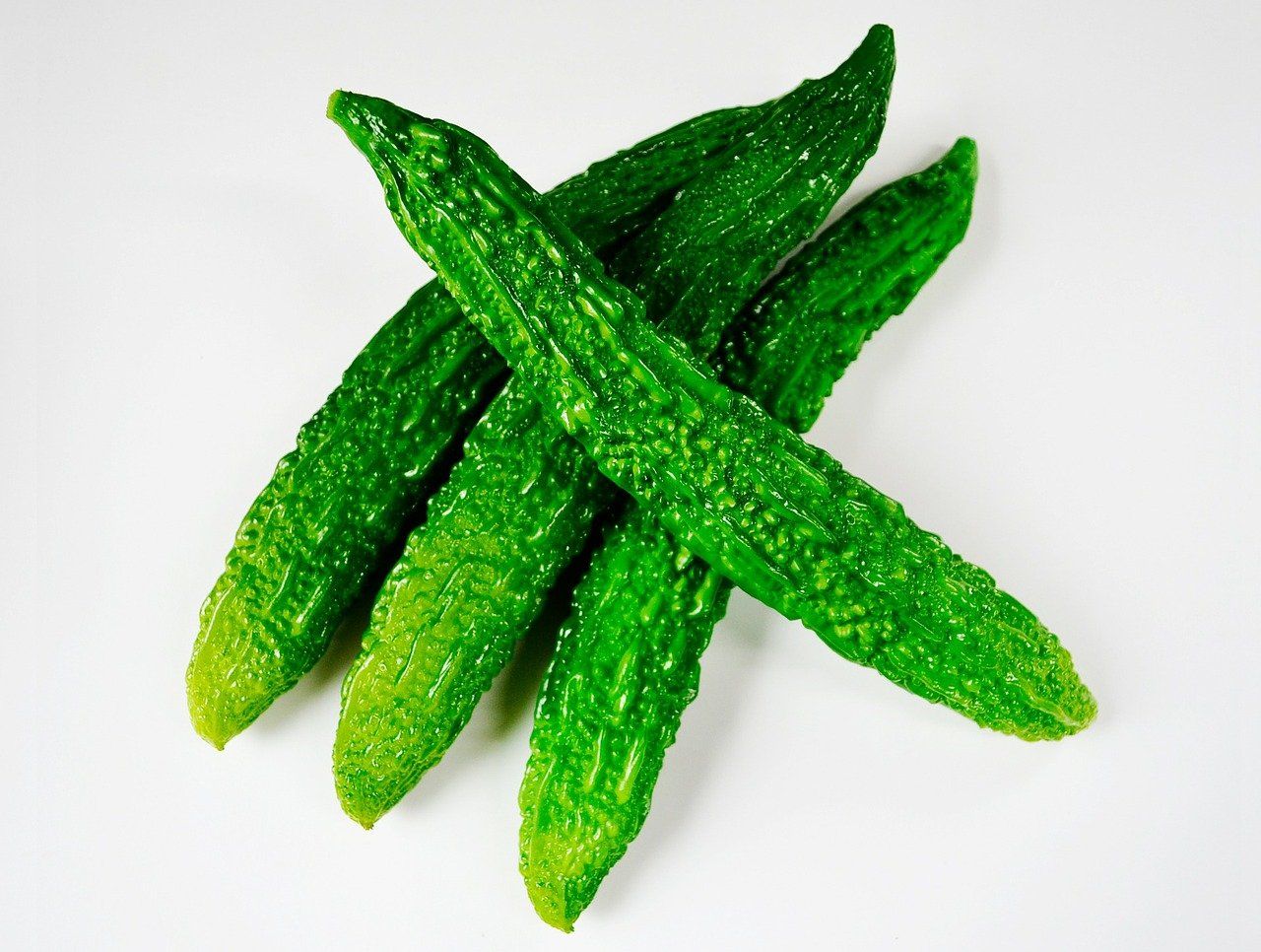 Four green cucumbers are crossed over each other on a white surface