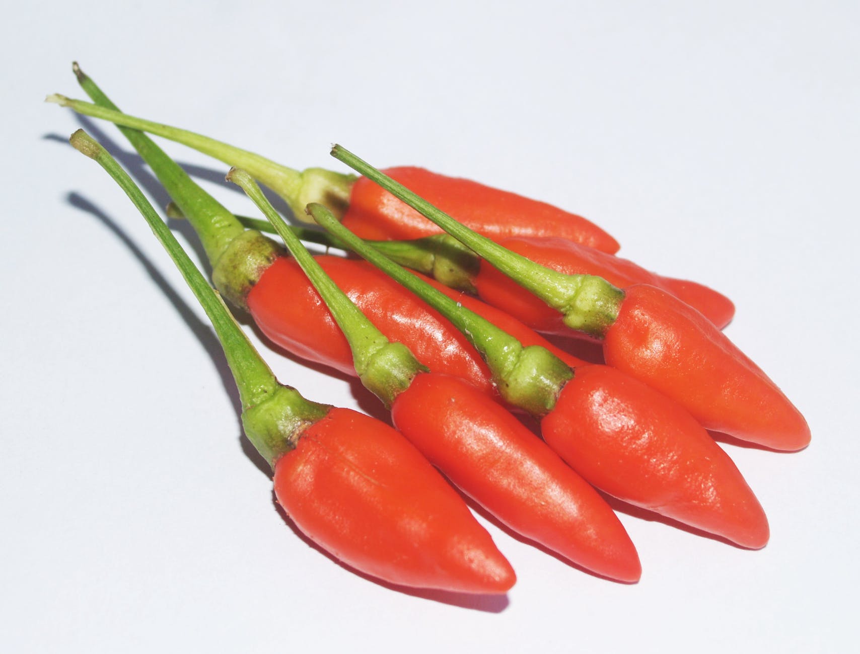 A bunch of red peppers with green stems on a white surface
