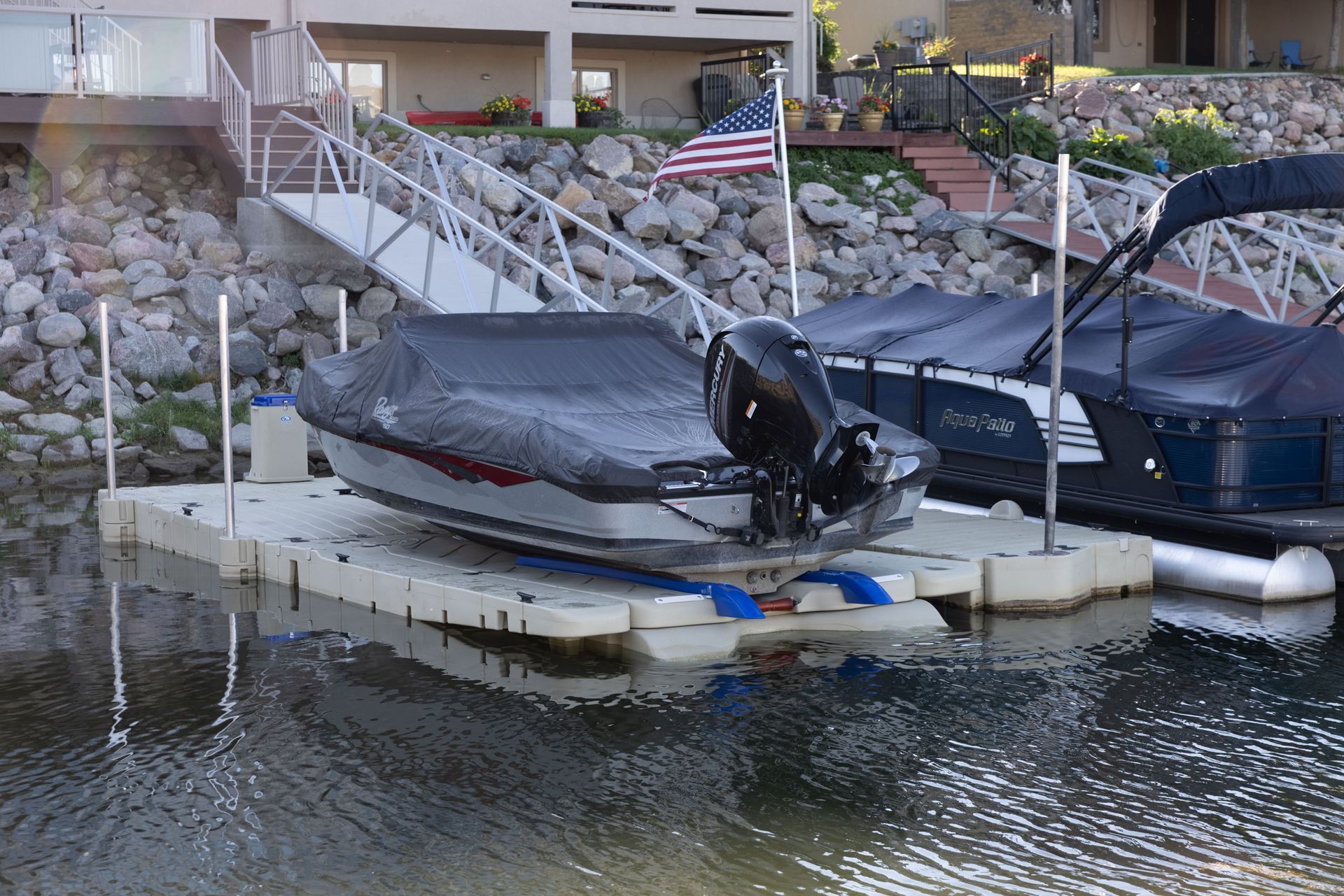 Boat on a floating dock, covered, with stairs to a house. American flag visible.