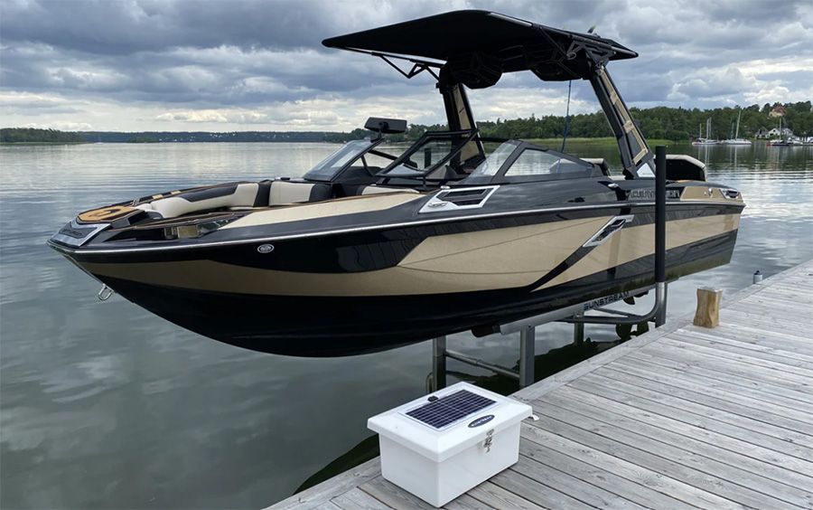 Boat on a lift at a dock. Black and tan boat with a black canopy in a lake setting under cloudy skies.