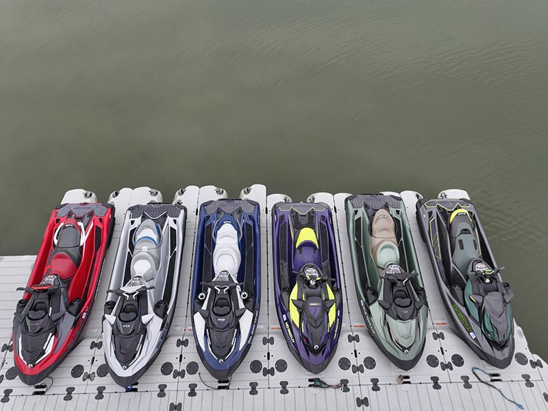 Six colorful jet skis docked on a floating platform against a backdrop of calm water.