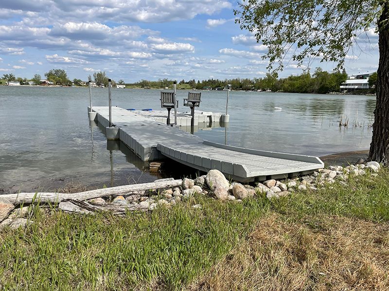 Gray dock with ramp in water, next to grassy shore, cloudy sky overhead.